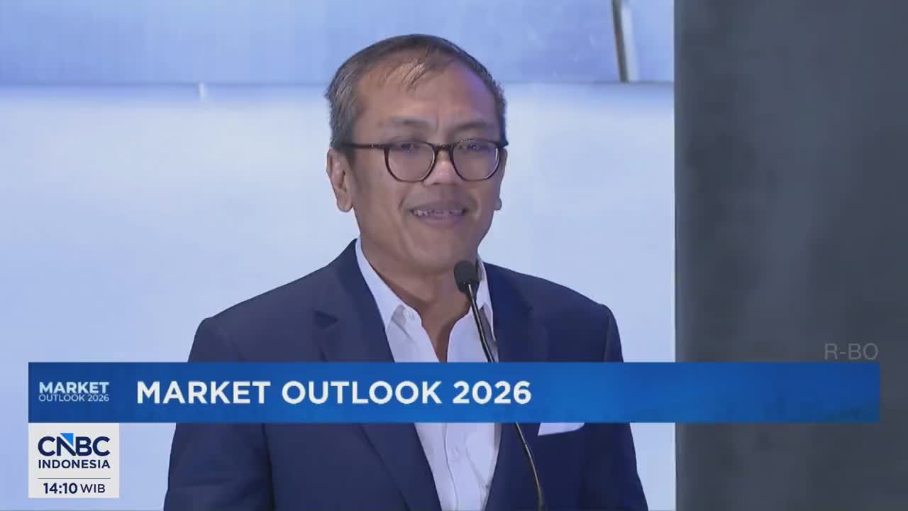 A man in a suit speaks into a microphone, his face illuminated by the lights. A blue banner behind him reads "MARKET OUTLOOK 2026" with the CNBC Indonesia logo. A man in a suit speaks into a microphone, his face illuminated by the lights. A blue banner behind him reads "MARKET OUTLOOK 2026" with the CNBC Indonesia logo.