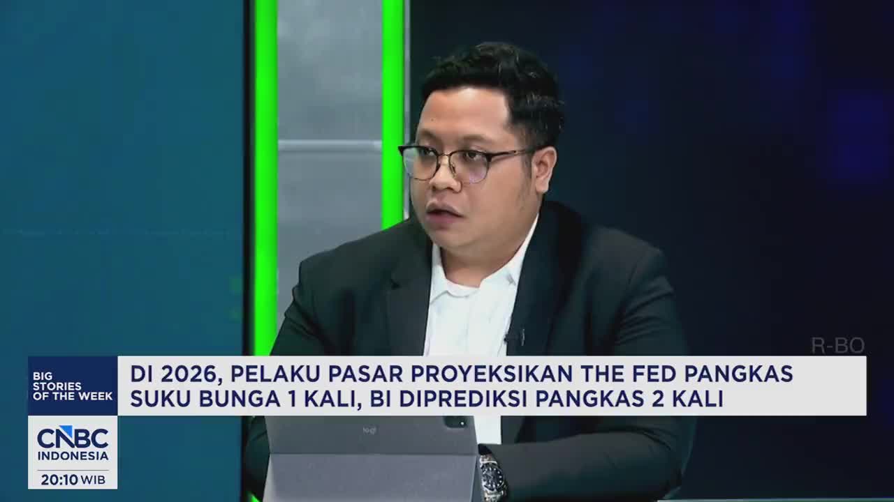 A man in a suit and glasses speaks, his gaze directed slightly off-camera. Behind him, a screen displays text from CNBC Indonesia. A man in a suit and glasses speaks, his gaze directed slightly off-camera. Behind him, a screen displays text from CNBC Indonesia.
