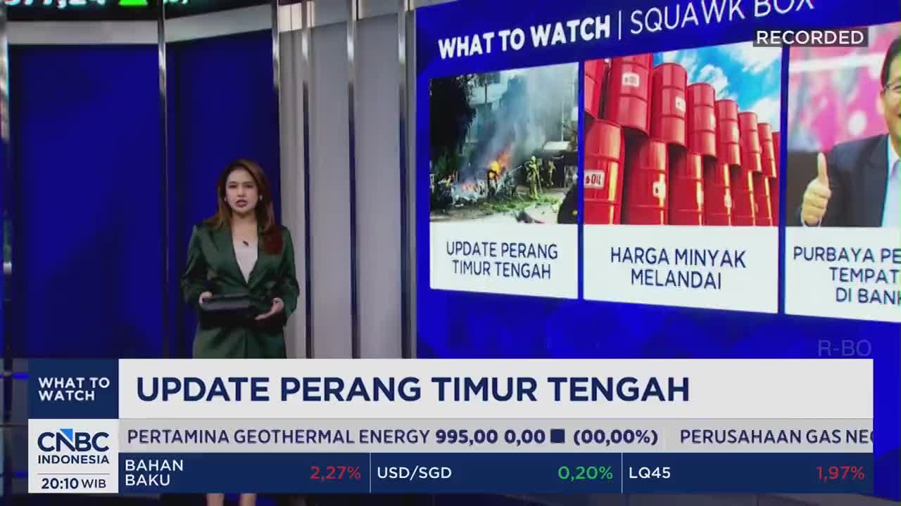 A woman in a green blazer stands before a large screen displaying news headlines from CNBC Indonesia. Flames erupt from a scene of destruction on the left, while a row of red oil barrels fills the center panel. A woman in a green blazer stands before a large screen displaying news headlines from CNBC Indonesia. Flames erupt from a scene of destruction on the left, while a row of red oil barrels fills the center panel.