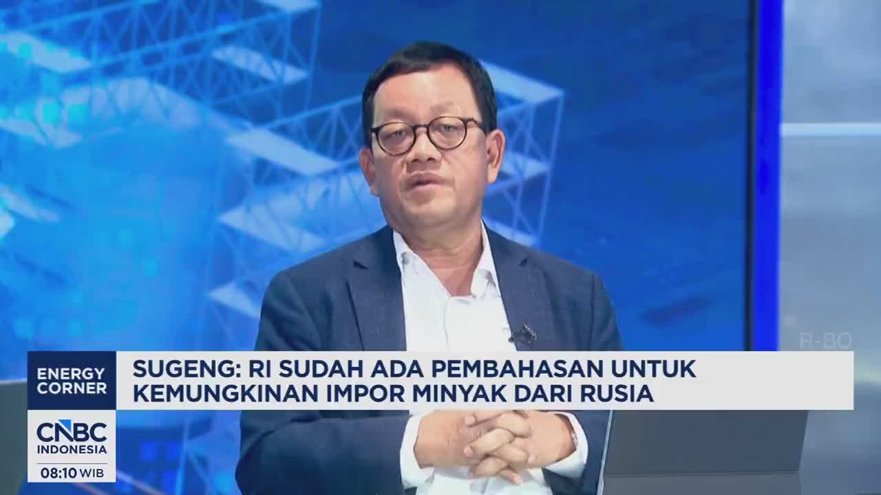A man in a suit and glasses speaks on CNBC Indonesia, his hands clasped. The screen behind him displays a blue, geometric pattern.