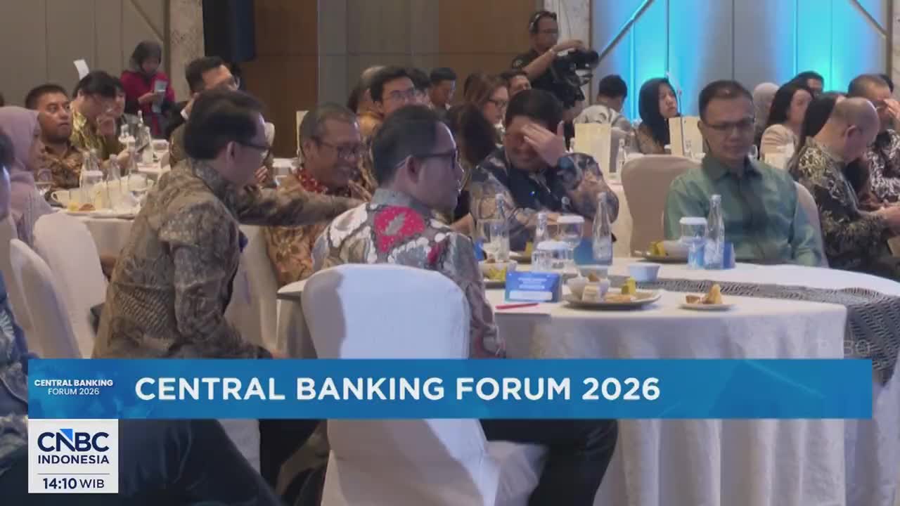 People are seated at round tables, attending a "Central Banking Forum 2026" event. A man in a green shirt looks forward, while others engage in conversation.