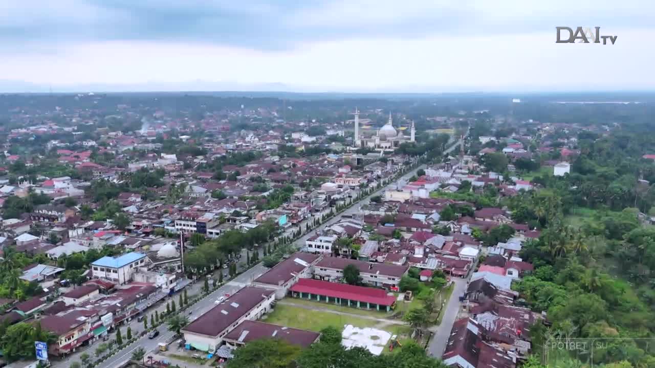 From this elevated perspective, a wide Indonesian town unfolds under a cloudy sky, with a prominent mosque and its minarets standing out. The DAAI TV logo sits in the corner, likely capturing a segment on the city's layout and daily life.
