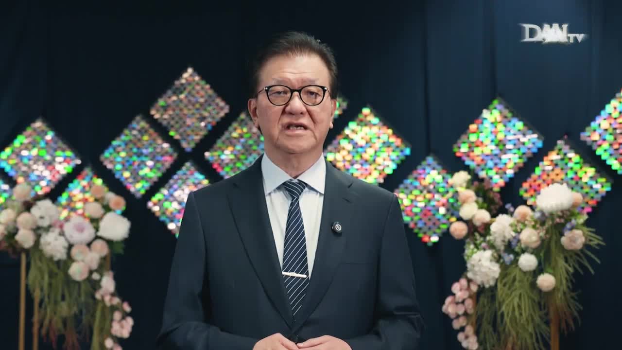 A man in a suit and tie is speaking, framed by floral arrangements and a backdrop of shimmering squares. The DAAI TV logo is visible in the corner.
