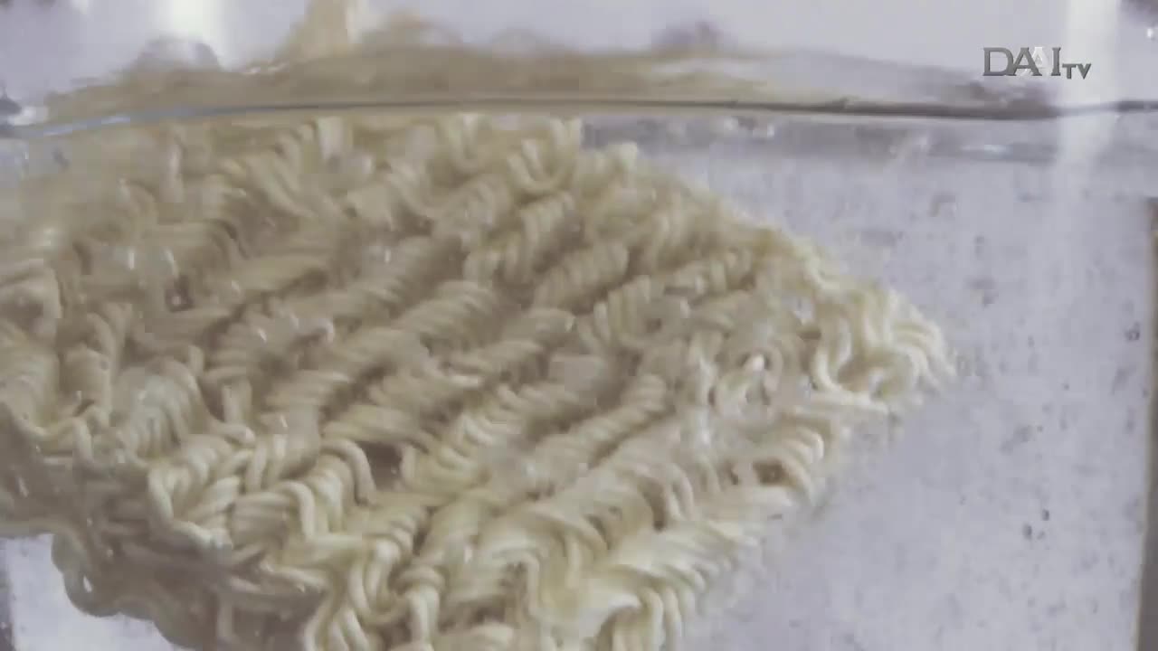A square of uncooked noodles bobs in clear, bubbling water. The DAAI TV logo sits in the corner as the pasta slowly softens.
