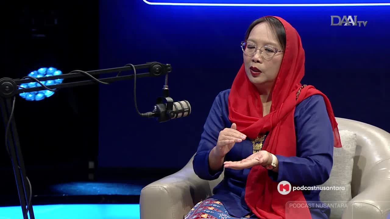 A woman in a red headscarf gestures with her hands as she speaks, seated in front of a microphone on a DAAI TV set. The podcast logo is visible in the corner.
