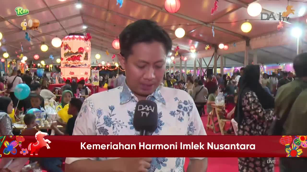 A reporter stands before a crowd gathered under a tent decorated with lanterns. Families mill about, enjoying the festive atmosphere of the Imlek celebration. A reporter stands before a crowd gathered under a tent decorated with lanterns. Families mill about, enjoying the festive atmosphere of the Imlek celebration.