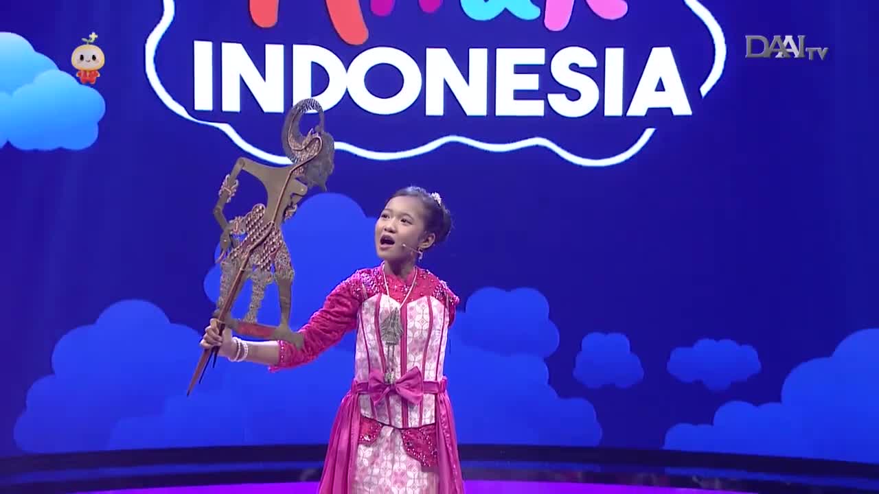 A young girl in a vibrant pink outfit holds up a wayang kulit puppet, its intricate details catching the light. She's on a stage, likely for a DAAI TV broadcast in Indonesia, with the word "INDONESIA" emblazoned behind her. A young girl in a vibrant pink outfit holds up a wayang kulit puppet, its intricate details catching the light. She's on a stage, likely for a DAAI TV broadcast in Indonesia, with the word "INDONESIA" emblazoned behind her.