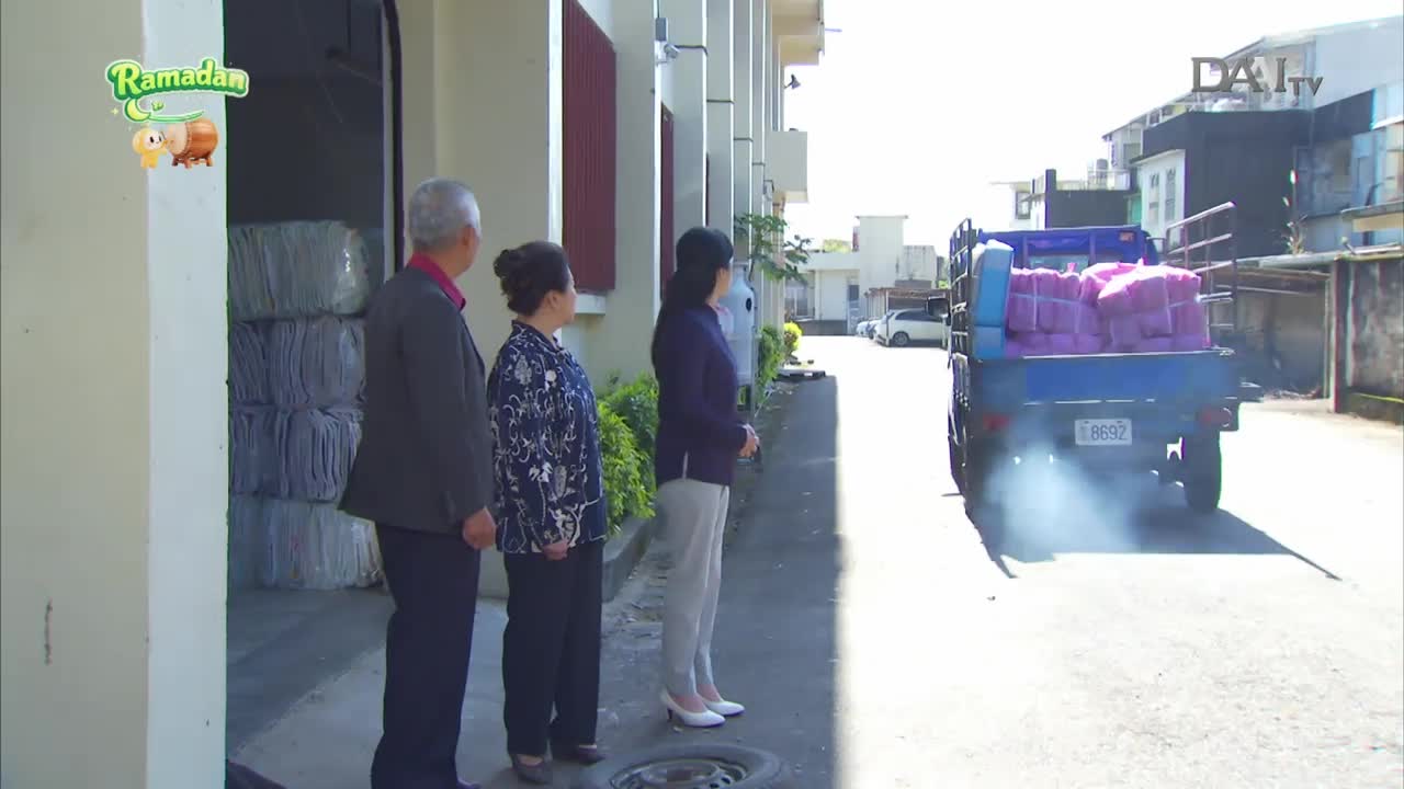 A blue truck, piled high with purple-wrapped packages, pulls away, leaving a trail of exhaust. Three people stand watching it go, their faces turned towards the departing vehicle.