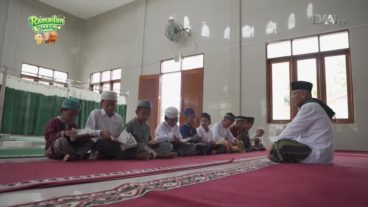 Children in white caps sit cross-legged on a red carpet, engrossed in their books. An elder, also in traditional attire, faces them, likely guiding their Ramadan studies.