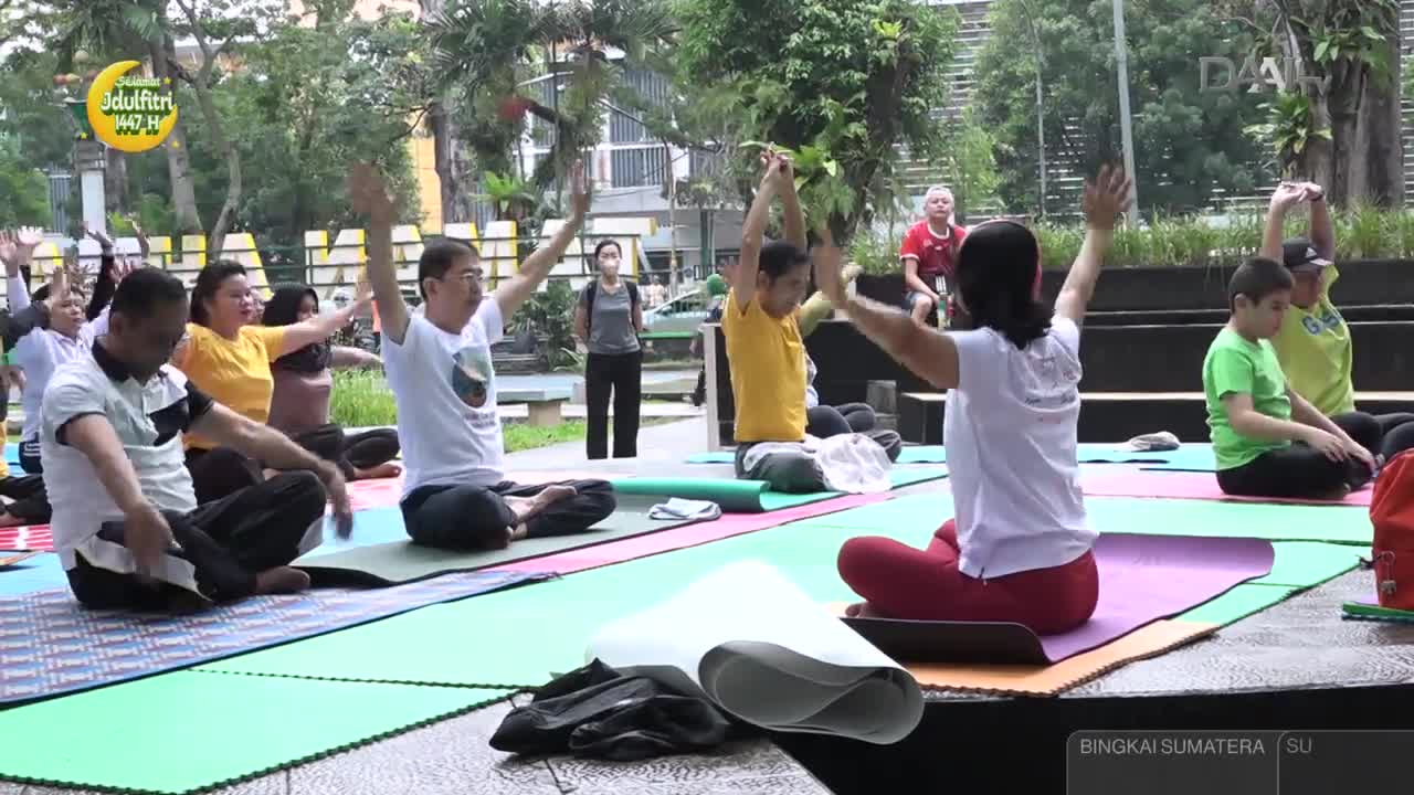A group of people are sitting cross-legged on mats, raising their arms towards the sky. The DAAI TV logo is visible in the background, suggesting this is a broadcast event.