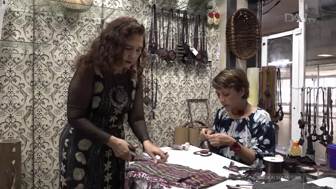 A woman with curly hair carefully cuts a patterned fabric with scissors. Beside her, another woman works with thread and beads, her hands busy with intricate detail. A woman with curly hair carefully cuts a patterned fabric with scissors. Beside her, another woman works with thread and beads, her hands busy with intricate detail.