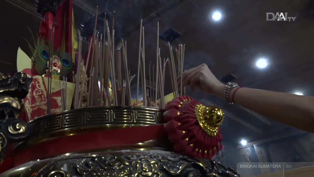 A hand carefully places an incense stick into an overflowing censer, wisps of smoke rising around the many already lit. This ritual unfolds within a temple, likely in North Sumatra, as indicated by the DAAI TV broadcast. A hand carefully places an incense stick into an overflowing censer, wisps of smoke rising around the many already lit. This ritual unfolds within a temple, likely in North Sumatra, as indicated by the DAAI TV broadcast.