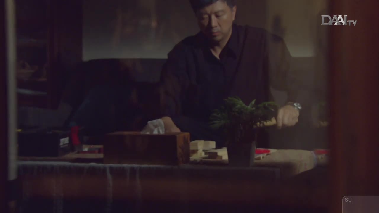 A man in a dark shirt leans over a table, his hands busy with something small. He's in a dimly lit room, the DAAI TV logo visible in the corner.