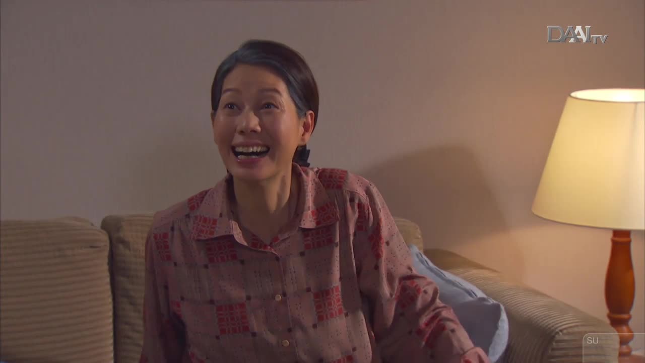 A woman in a patterned shirt laughs heartily while sitting on a couch. The DAAI TV logo appears in the upper right corner.