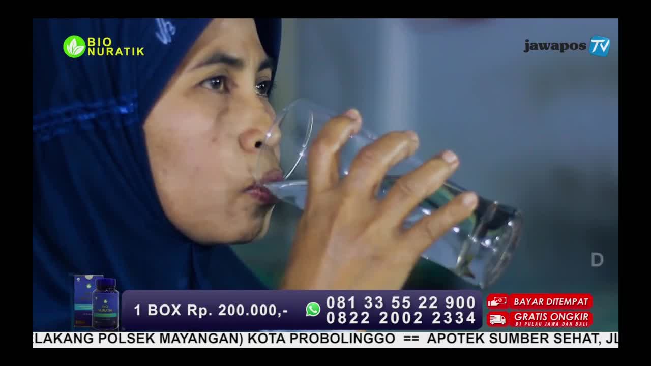 A woman wearing a hijab is tilting her head back, drinking from a clear glass. The Jawa Pos TV logo is visible in the corner, and an advertisement for a product called Bio Nuratik is displayed below.
