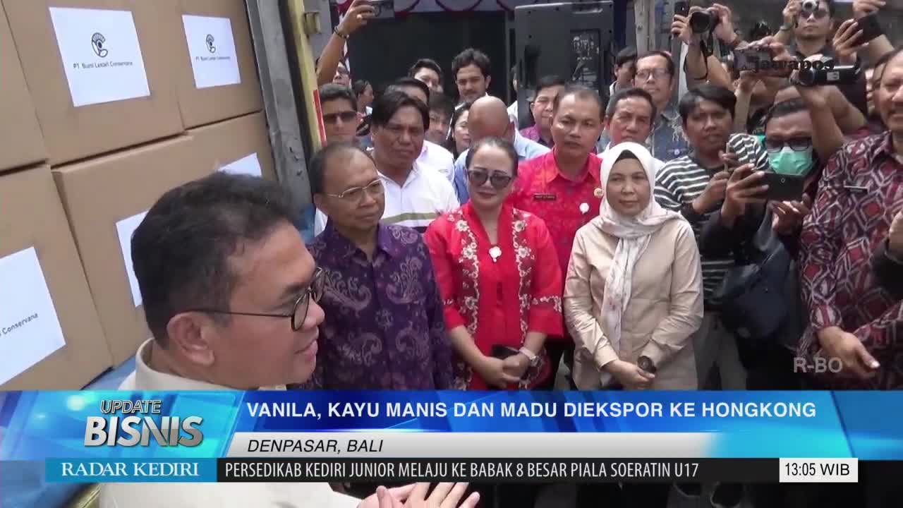 A crowd, many with phones raised, surrounds a group of people in front of a truck. The Jawa Pos TV screen displays "VANILA, KAYU MANIS DAN MADU DIEKSPOR KE HONGKONG," with the location listed as Denpasar, Bali.
