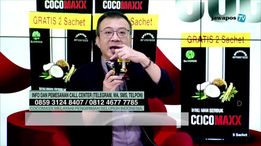 A man in glasses gestures with a small packet of "COCOMAXX" drink, while the Jawa Pos TV screen displays the product's packaging. Below, a call center number is visible, offering delivery across Indonesia.

