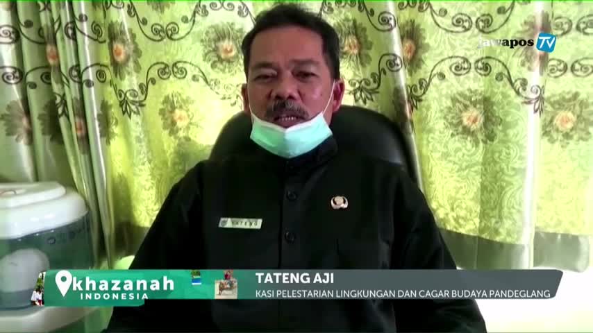 A man in a black shirt and a face mask speaks earnestly, his words broadcast on Jawa Pos TV. The screen displays his name and title, identifying him as an official from Pandeglang, Indonesia.
