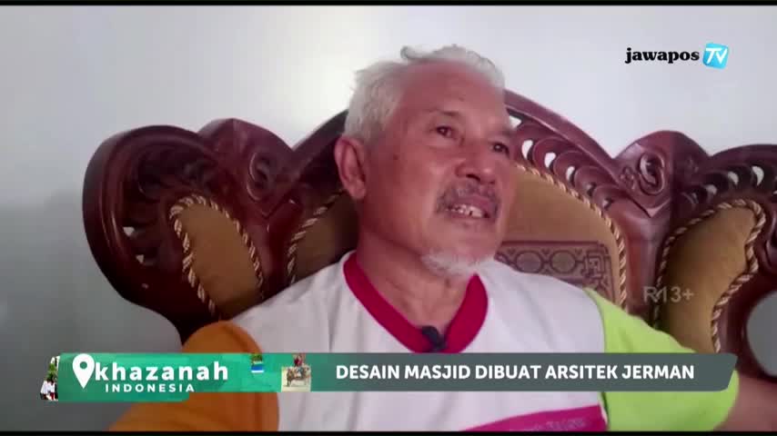 An older man with gray hair and a mustache is speaking, framed by an ornate chair. The Jawa Pos TV logo is visible, and a graphic at the bottom of the screen mentions a mosque design by a German architect.
