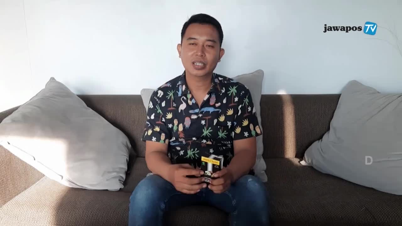 The man, seated on a couch, is speaking directly to the camera, a Jawa Pos TV logo visible in the background. He's holding a small box, presumably for a product review, as he gestures with it.
The man, seated on a couch, is speaking directly to the camera, a Jawa Pos TV logo visible in the background. He's holding a small box, presumably for a product review, as he gestures with it.