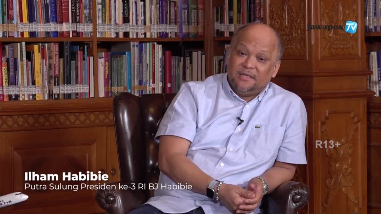 Ilham Habibie, the eldest son of Indonesia's third president, is seated in a leather chair, speaking on Jawa Pos TV. Behind him, a wall of books fills the frame, and the Jawa Pos TV logo is visible in the upper right corner.
Ilham Habibie, the eldest son of Indonesia's third president, is seated in a leather chair, speaking on Jawa Pos TV. Behind him, a wall of books fills the frame, and the Jawa Pos TV logo is visible in the upper right corner.