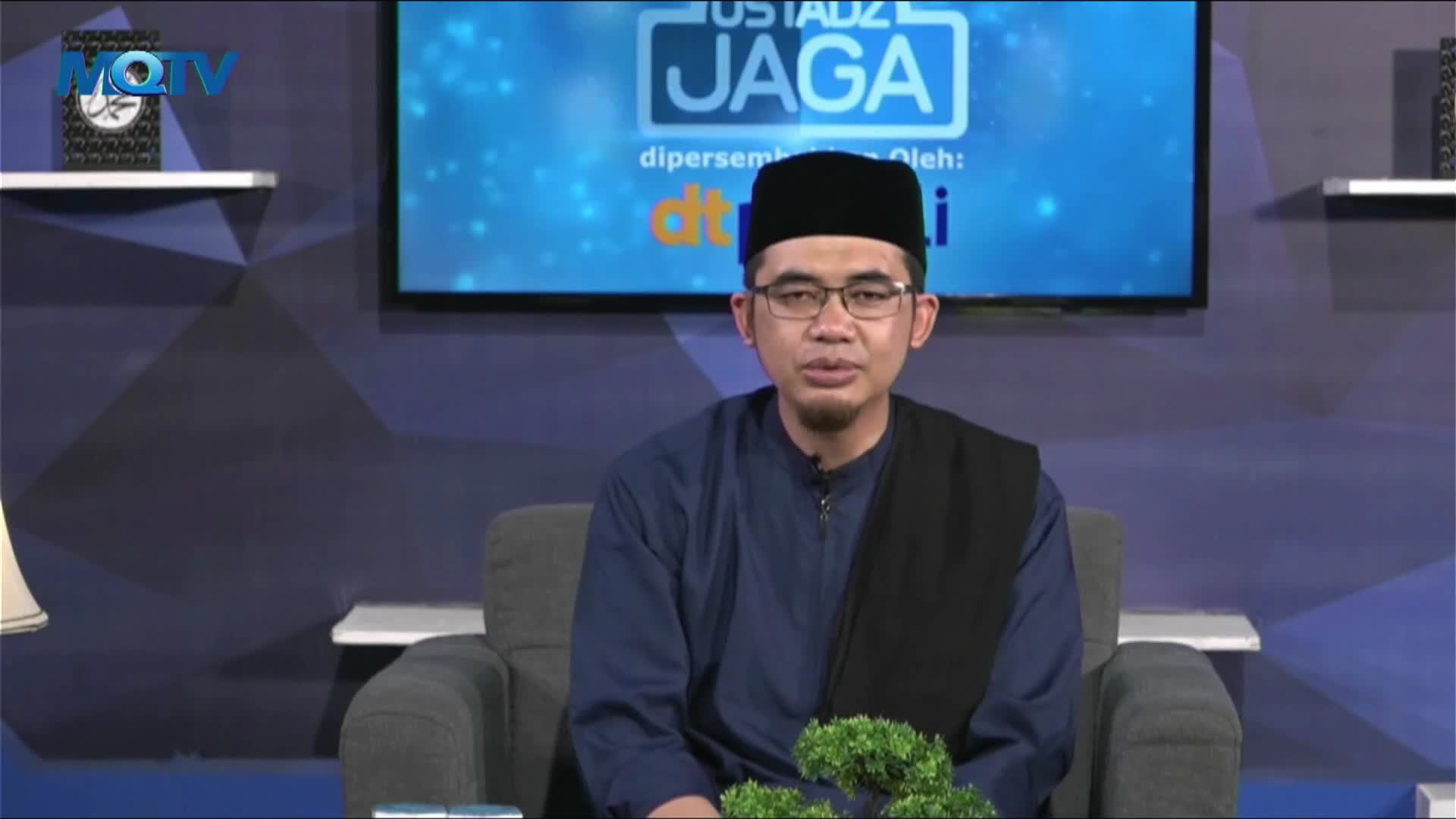 The man in the glasses and black cap sits in a studio chair, speaking directly to the camera. Behind him, the MQTV logo is visible on a shelf, and a screen displays the words "USTADZ JAGA."
