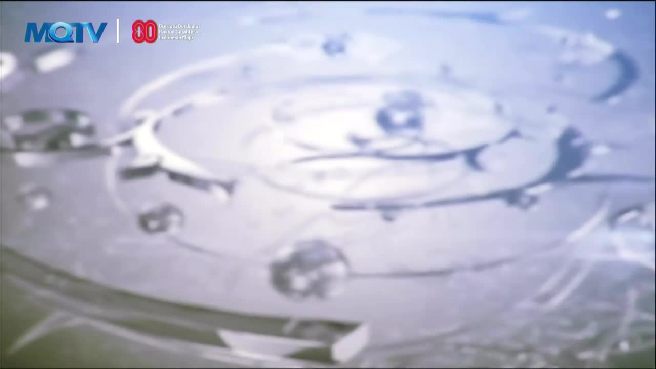 The MQTV logo is visible in the corner. The shot is focused on a blurry, circular object, possibly a machine part.
