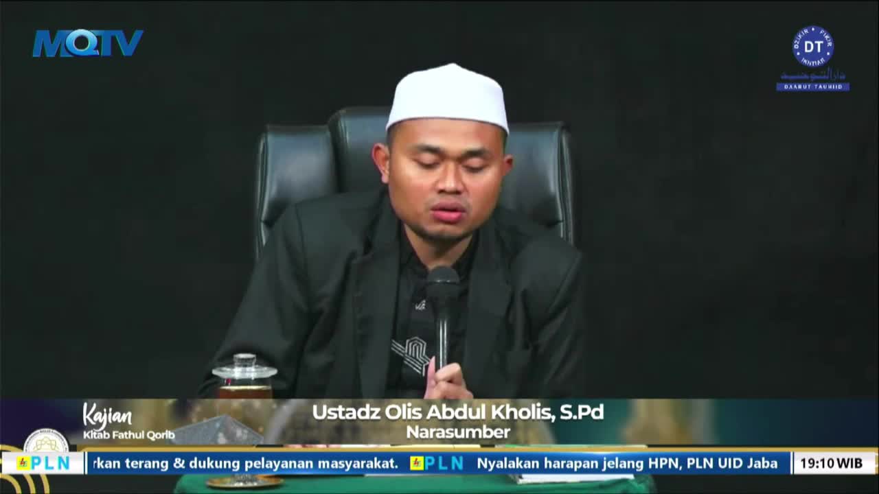 A man in a white cap and black jacket is speaking into a microphone on a television set. Below, the MQTV logo and other Indonesian text are visible.
