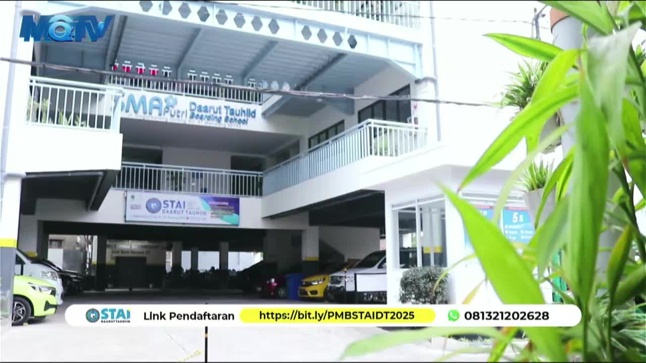 The MQTV logo sits in the corner, while a modern building with a sign for a boarding school fills the frame.  A few cars are parked in front, and green plants frame the right side of the shot.

