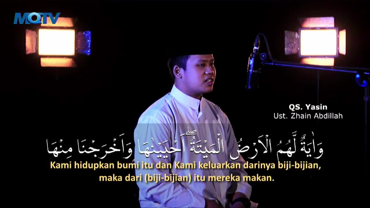 A man in a white shirt speaks into a microphone on a dark stage, with bright lights framing the scene. Arabic script and Indonesian translations appear below him, as the MQTV logo is visible in the corner.
