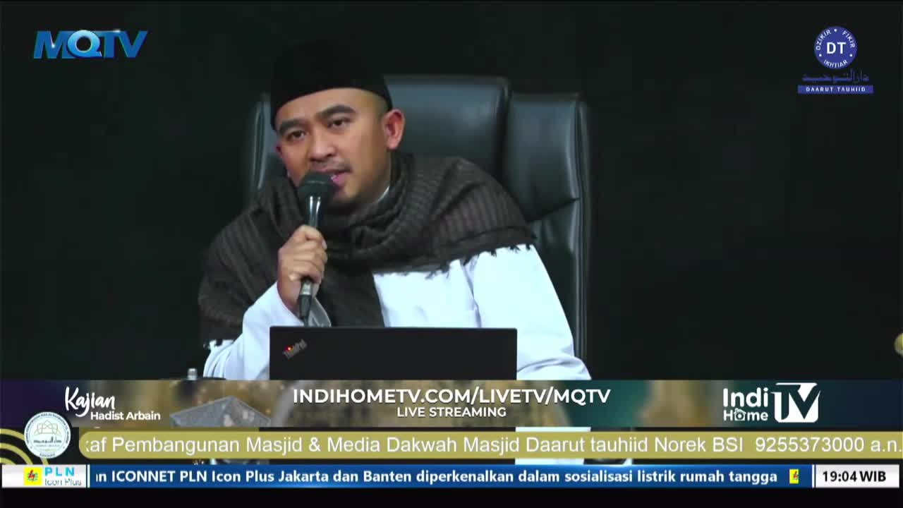 A man in a black cap and scarf speaks into a microphone, seated in front of a laptop. The MQTV logo is visible in the corner, and the broadcast is live streaming.
