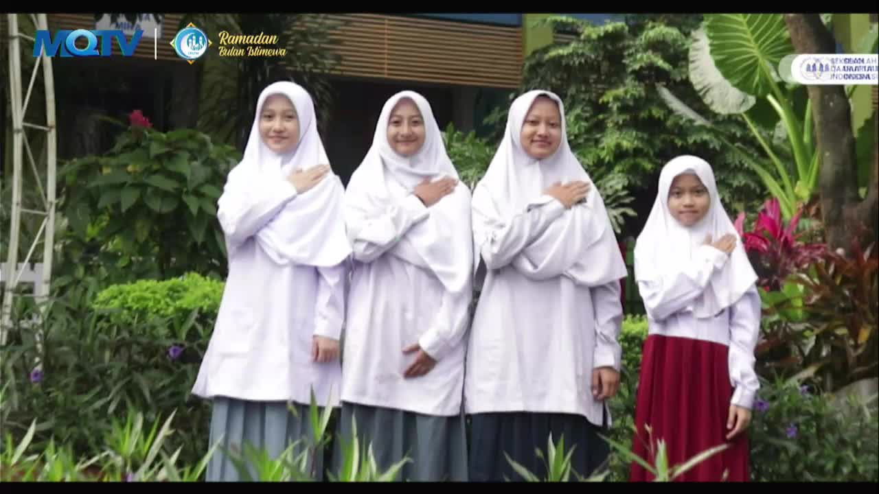 Four young women in white hijabs and school uniforms stand with their hands over their hearts. They are posing for a broadcast on MQTV, likely for a Ramadan program.