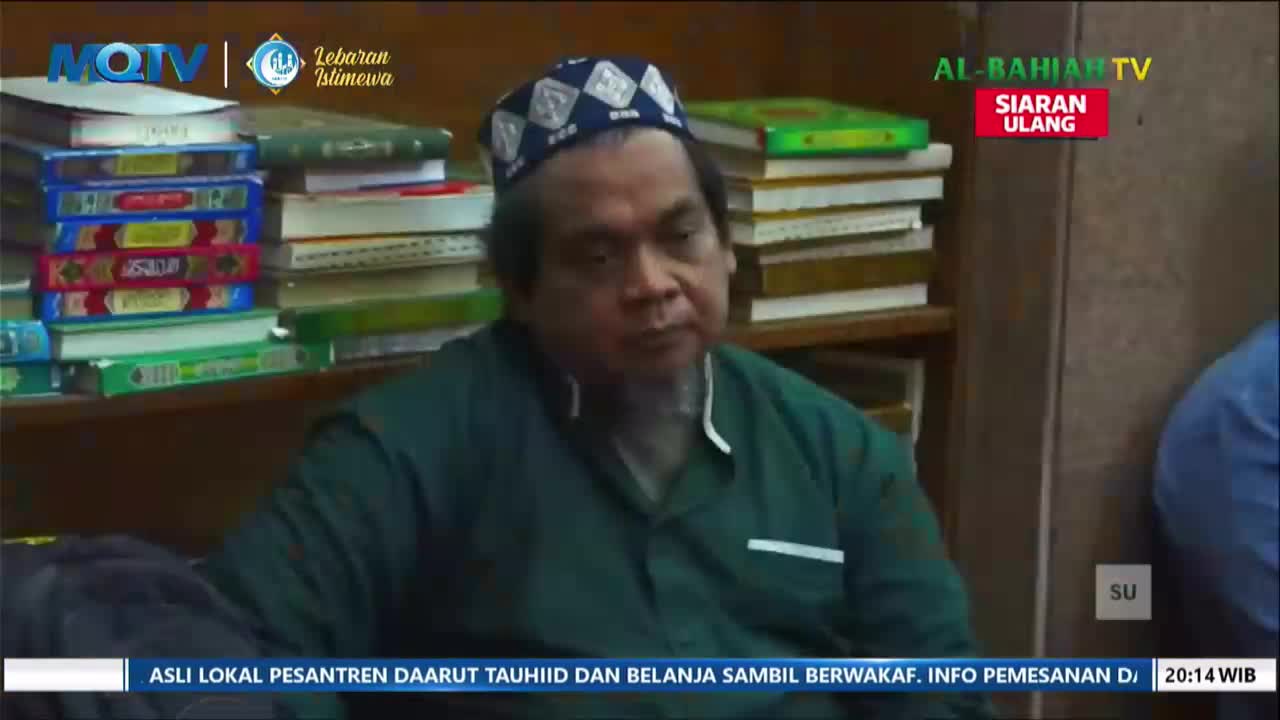 A man in a green shirt and a patterned cap sits in front of shelves packed with books. The MQTV logo is visible in the upper left corner.