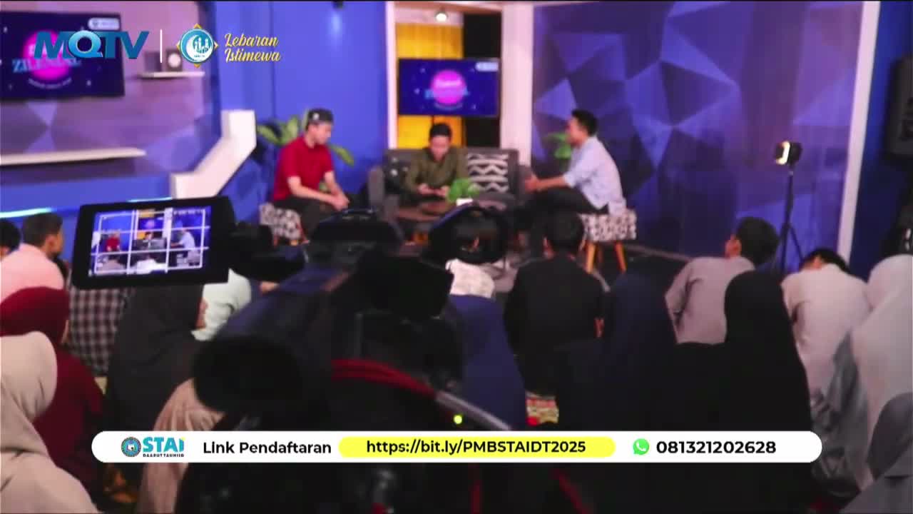 The studio lights illuminate three men in conversation on a raised platform, while a camera operator films them from the foreground.  The MQTV logo is visible on a screen behind the seated men, indicating a broadcast from Indonesia.