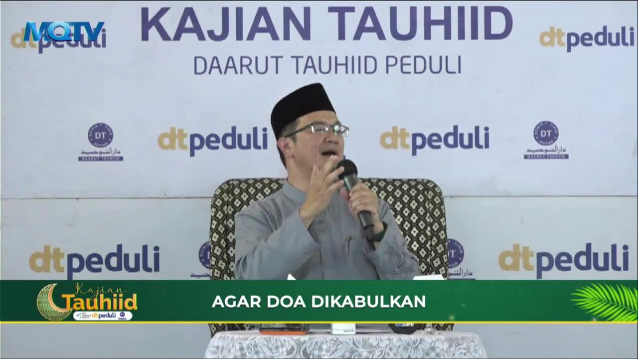 A man in a traditional cap and glasses speaks into a microphone, gesturing with his hands. The backdrop behind him displays the words "KAJIAN TAUHIID" and "DAARUT TAUHIID PEDULI," along with repeated logos.