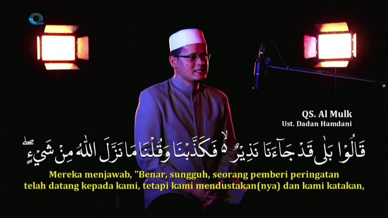 A man in a white peci and glasses speaks into a microphone, illuminated by studio lights. Arabic script, likely from the Quran, and its Indonesian translation appear on screen below him.
