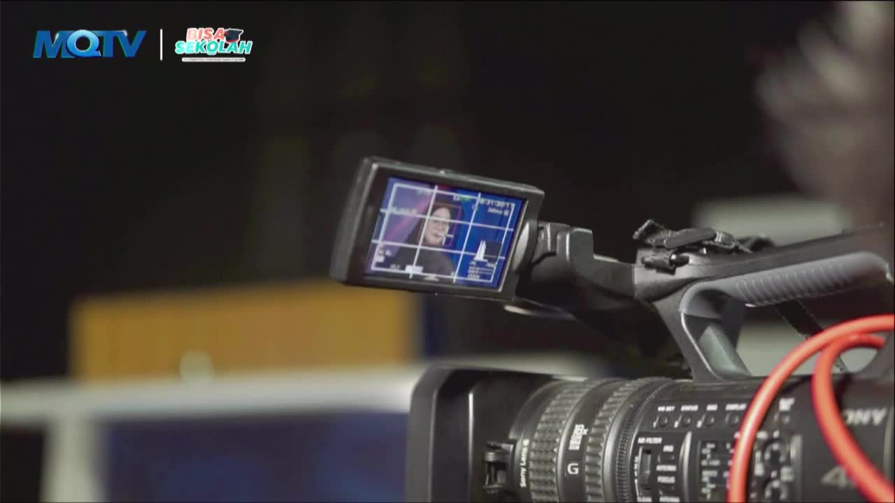 A camera operator films a presenter on the MQTV "Bisa Sekolah" program. The monitor shows the presenter's face framed by a grid.