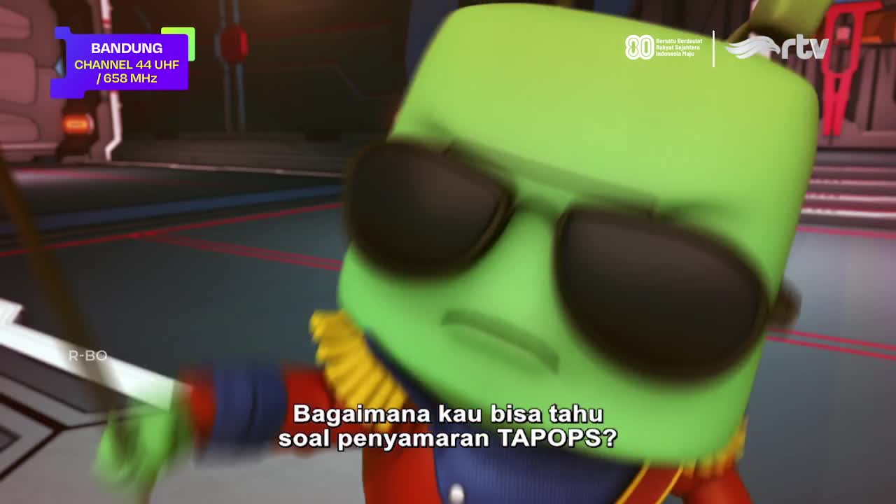 A green, square-headed character wearing sunglasses is in motion, its face slightly blurred. Indonesian text, along with the Rajawali TV logo, appears on screen.
