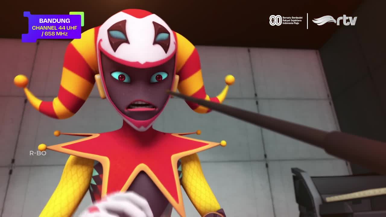 A jester-like character with a startled expression faces a dark, thin object. The scene is from Rajawali TV in Bandung, Indonesia, where the broadcast is coming from.
