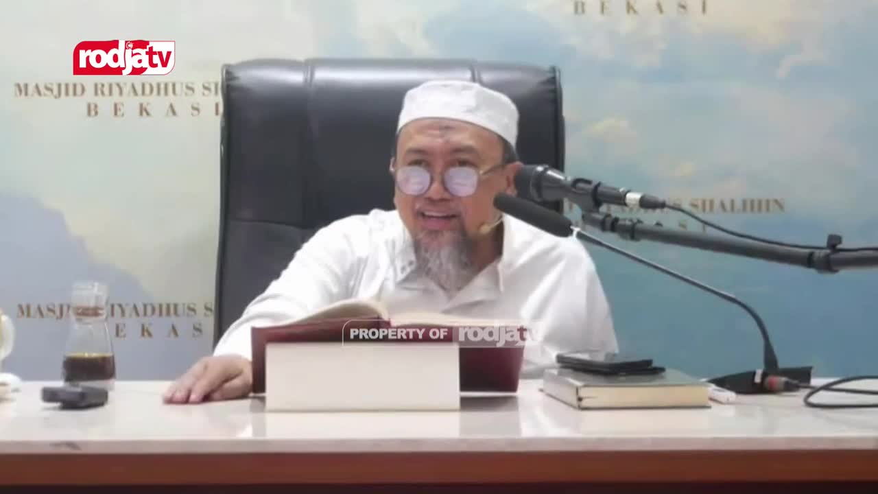A man in a white cap and glasses gestures while speaking, his voice amplified by a microphone. The Rodja TV logo is visible, and the backdrop shows a mosque in Bekasi, Indonesia.

