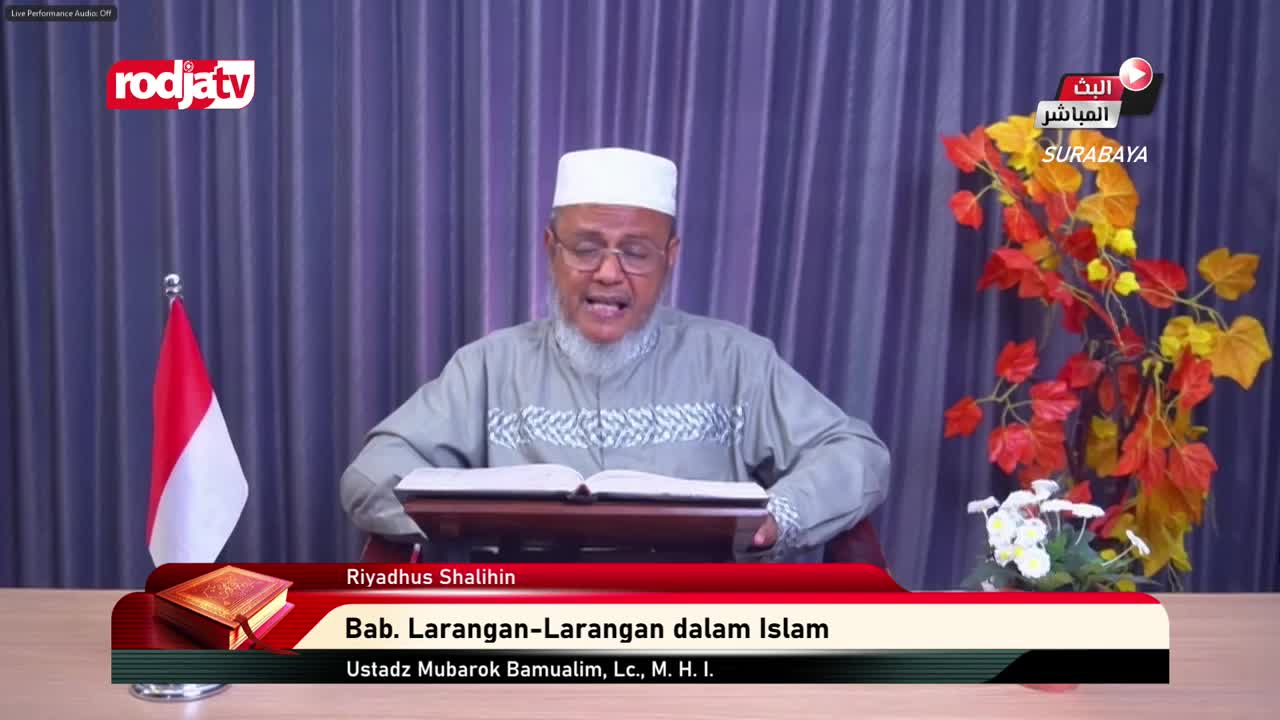 A man wearing a white cap and glasses is speaking, reading from an open book on a stand. The broadcast from Rodja TV in Surabaya, Indonesia, features the Indonesian flag to the left.
