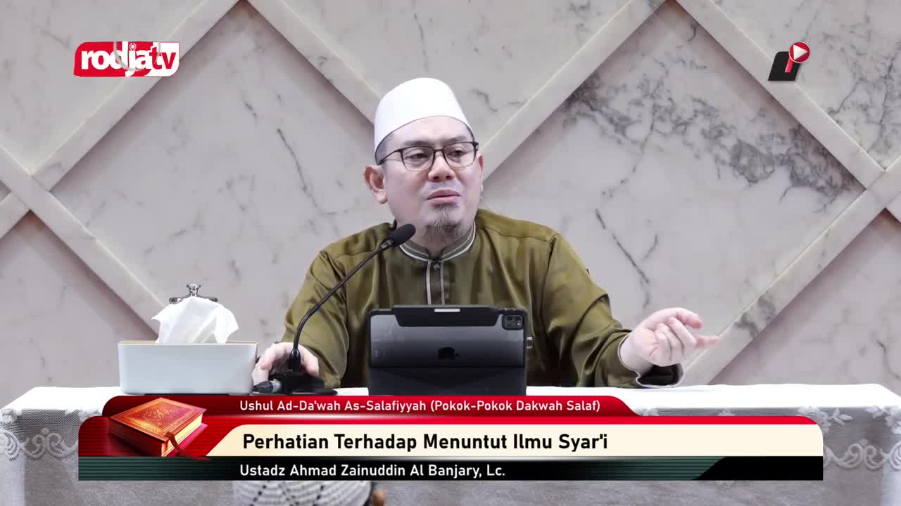 A man in a white cap and glasses gestures with his right hand while speaking into a microphone. The Rodja TV logo is visible in the corner, and a banner below lists the topic of his lecture in Indonesian.
