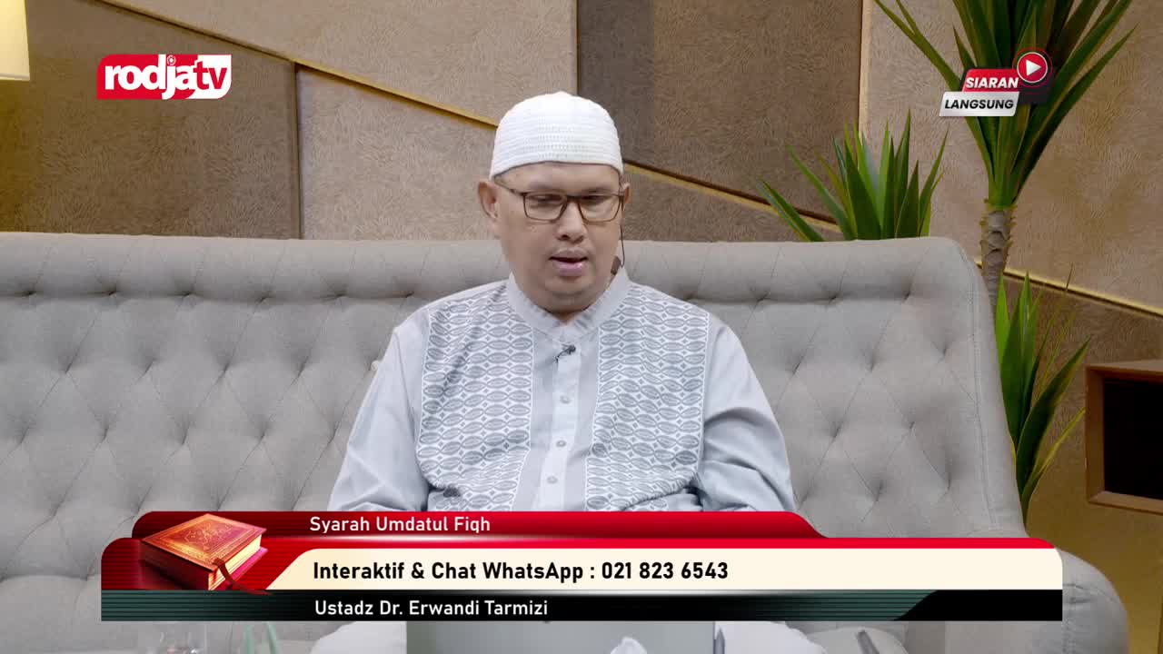 The man in the white cap and glasses is speaking, seated on a gray couch. A Rodja TV program in Indonesia is underway, with a graphic advertising "Syarah Umdatul Fiqh" at the bottom of the screen.
