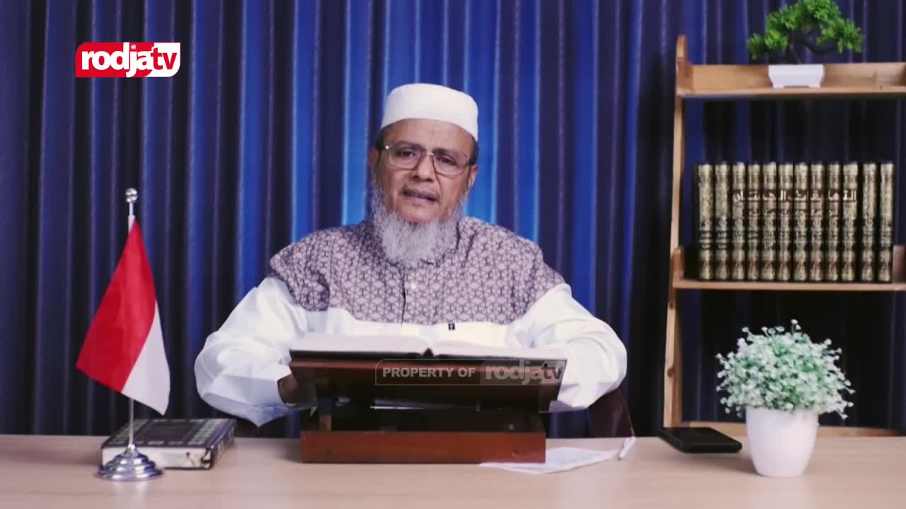 A man in a white cap and beard sits at a desk, speaking into a camera. Behind him, the Indonesian flag stands beside a small book, and the Rodja TV logo is visible in the corner.
