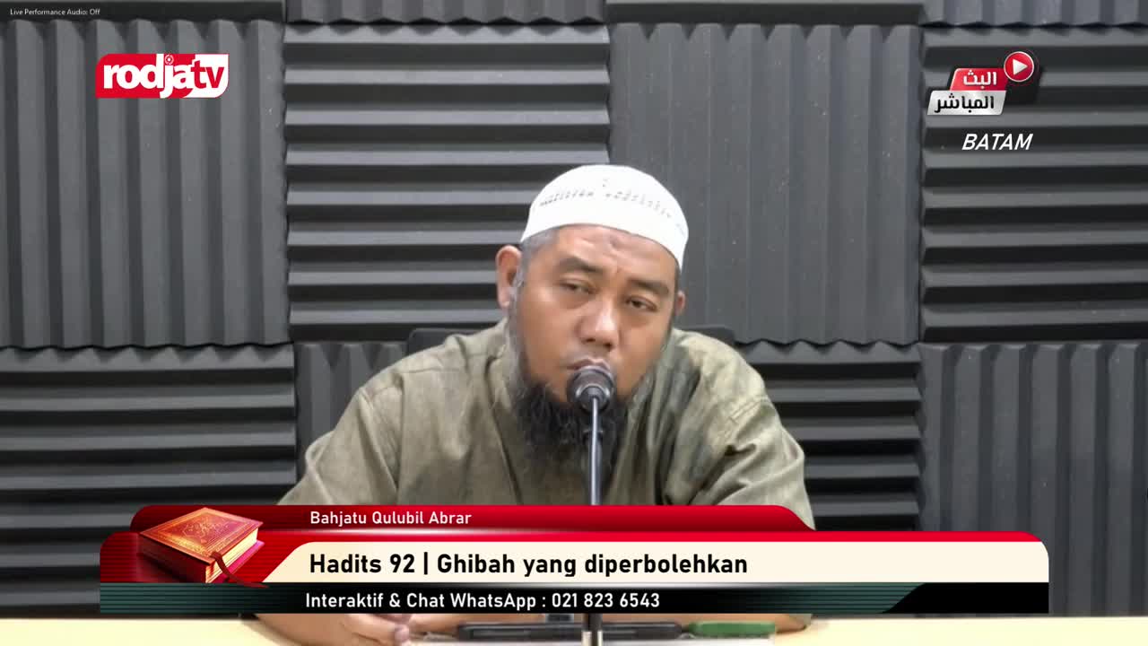 A man wearing a white cap speaks into a microphone, his face lit by studio lights. The Rodja TV logo is visible in the top left corner, and a graphic at the bottom identifies the program's topic.
