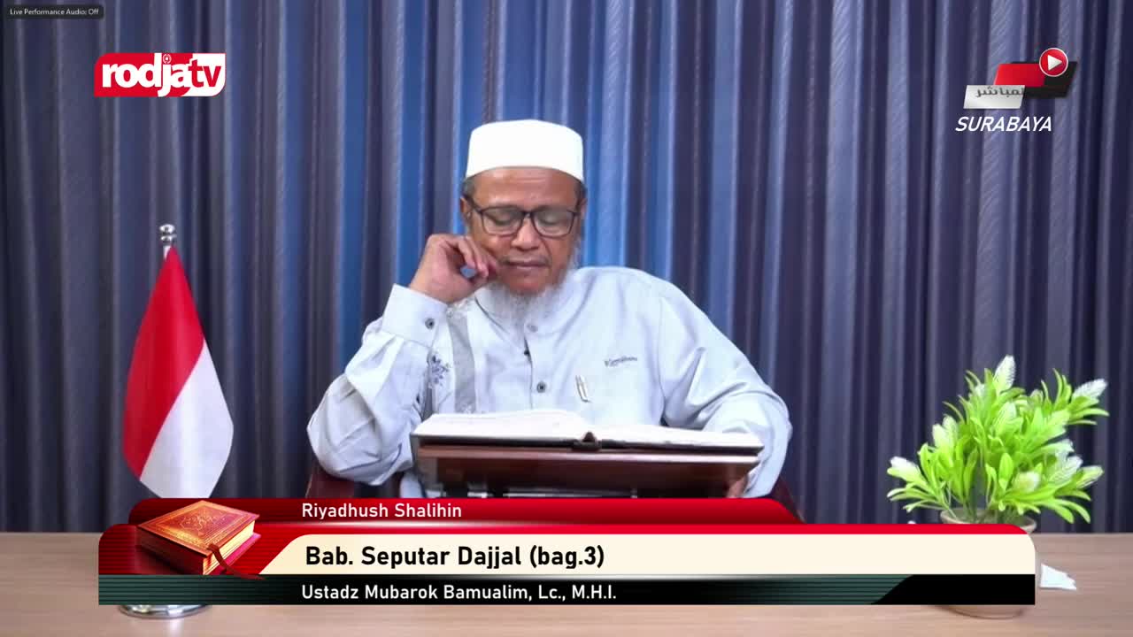 An Indonesian flag stands to the left of a man in a white cap, who is reading from a book on a wooden stand. The Rodja TV logo is visible in the upper left corner, and a lower third graphic identifies the speaker and topic.
