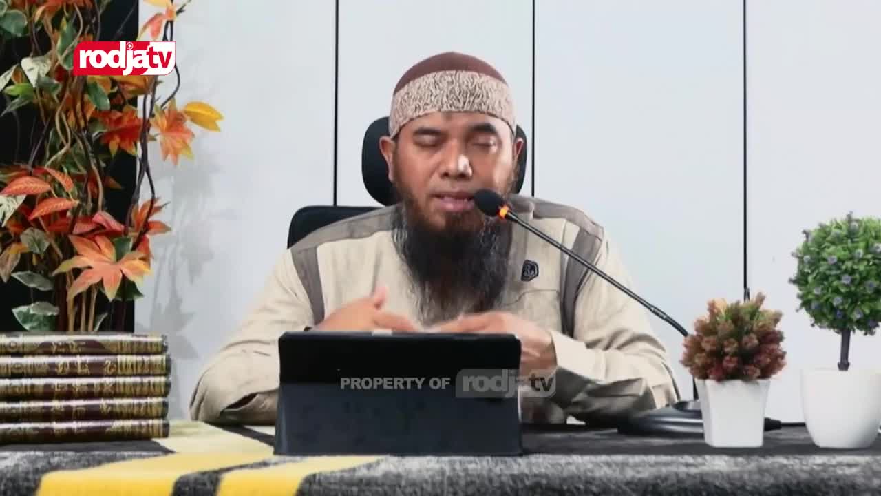 A man with a long black beard speaks into a microphone, gesturing with his hands. The Rodja TV logo is visible in the corner as he addresses the camera.
