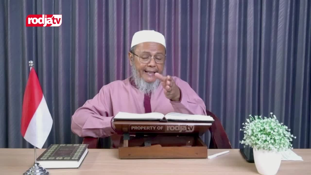 The man in the white cap gestures with his right hand, speaking animatedly while reading from an open book. The Indonesian flag stands to his left, and the Rodja TV logo is in the corner.
