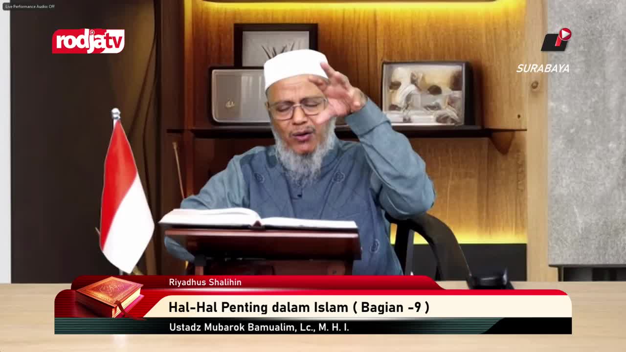 A man with a white cap and beard gestures with his right hand as he speaks, his left hand resting on an open book. The Indonesian flag stands to his left, and the Rodja TV logo is visible in the upper left corner.

