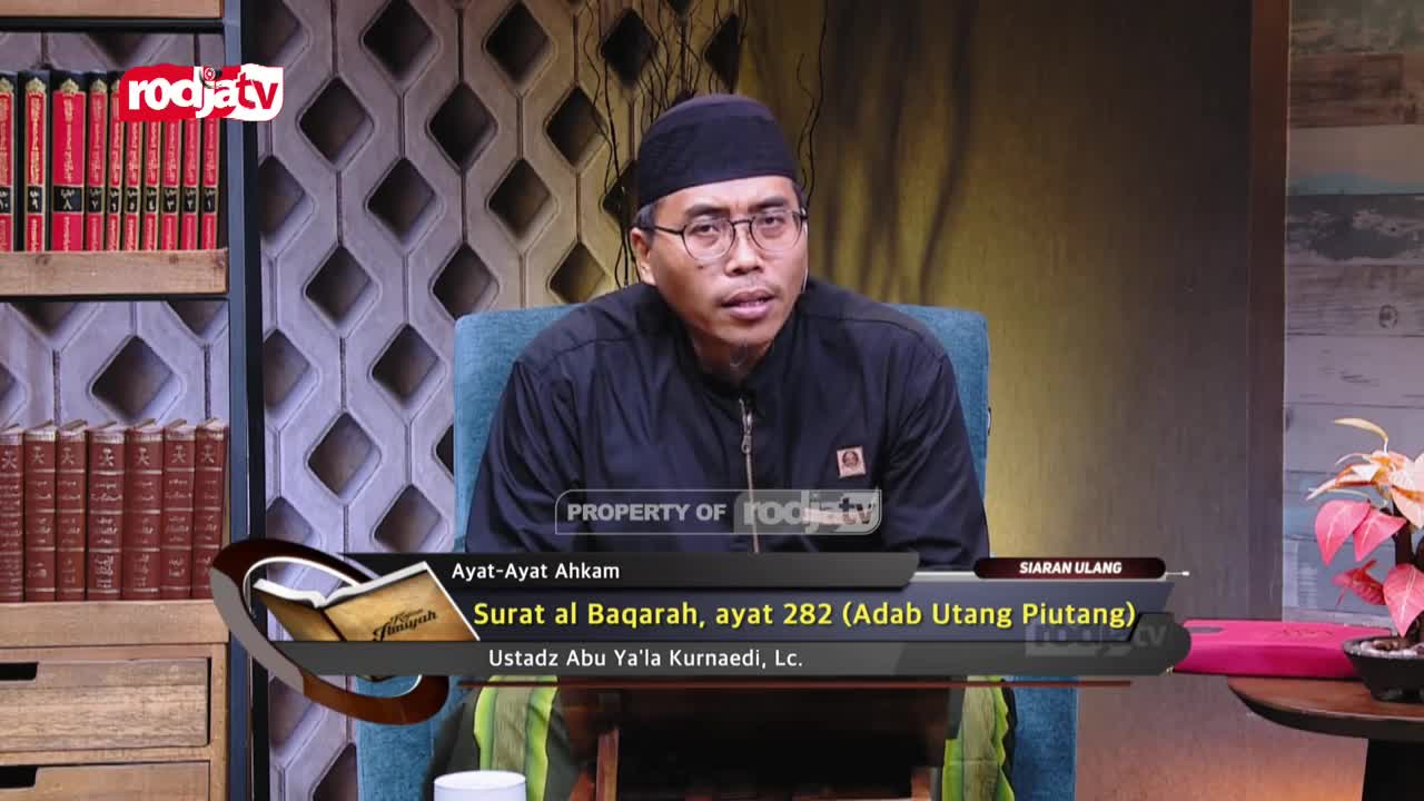 A man in a black peci and glasses speaks from behind a desk, his voice broadcast by Rodja TV. The screen displays the title "Surat al Baqarah, ayat 282 (Adab Utang Piutang)" and the speaker's name, Ustadz Abu Ya'la Kurnaeidi, Lc. A man in a black peci and glasses speaks from behind a desk, his voice broadcast by Rodja TV. The screen displays the title "Surat al Baqarah, ayat 282 (Adab Utang Piutang)" and the speaker's name, Ustadz Abu Ya'la Kurnaeidi, Lc.